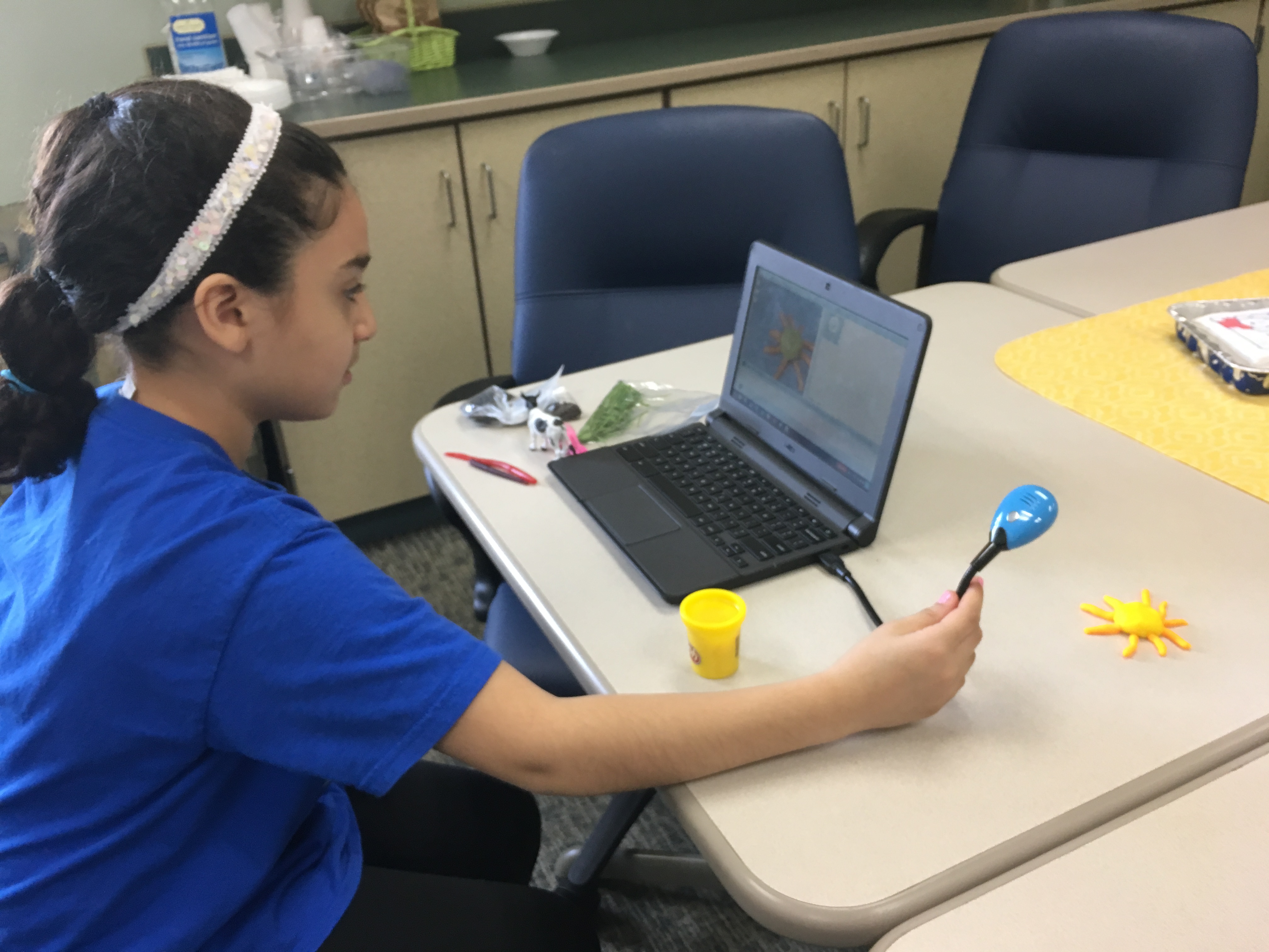 a female student uses a webcam and a chromebook to take pictures of a clay sun