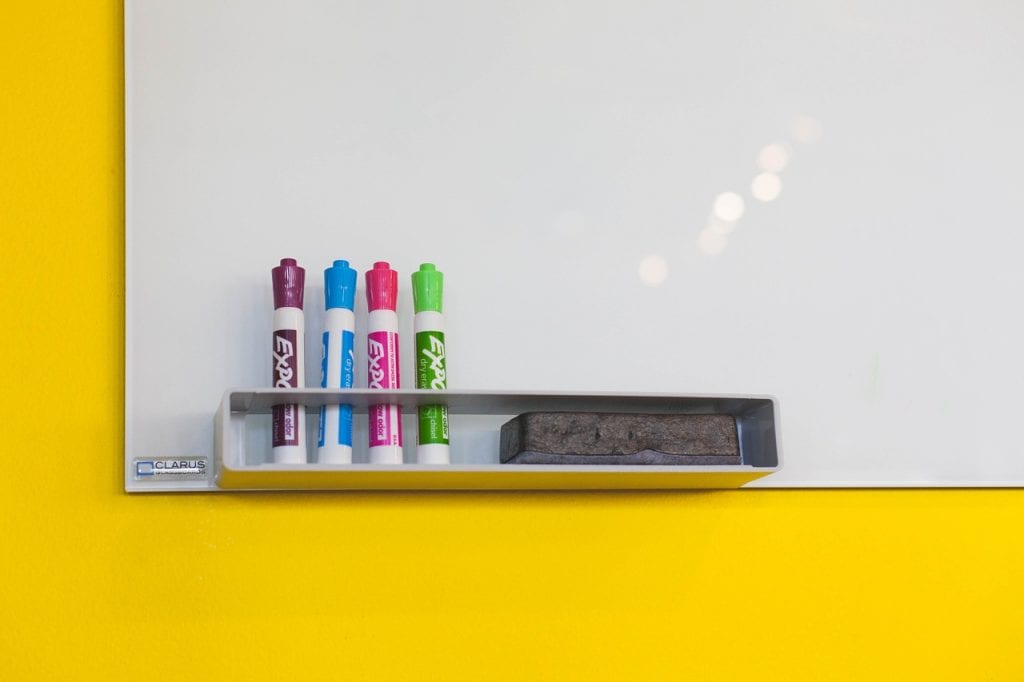 whiteboard with 4 colored markers and an eraser against a yellow background