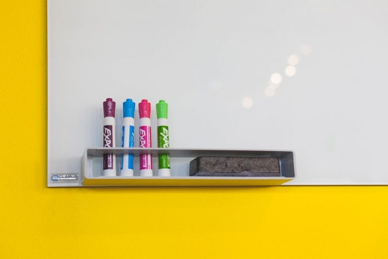 whiteboard with 4 colored markers and an eraser against a yellow background