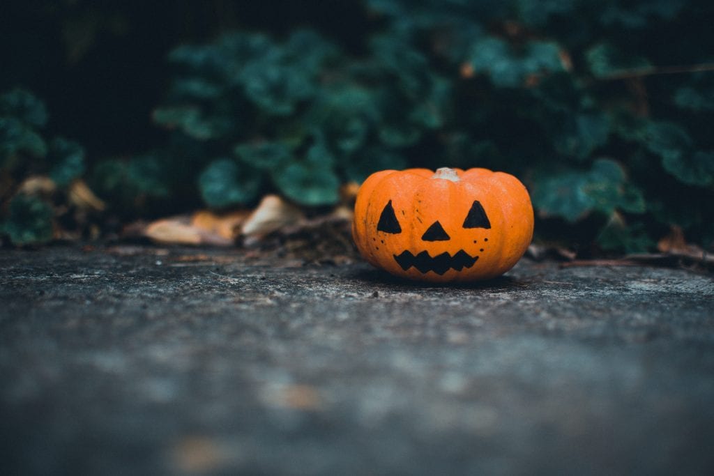 tiny jack o lantern sitting on the sidewalk in front of a tree