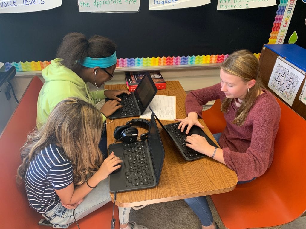 three girls sit at a booth and work on their computers