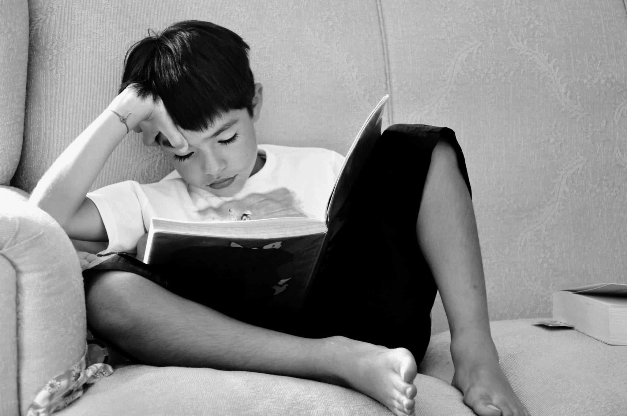 black and white image of a boy reading a book casually on the couch