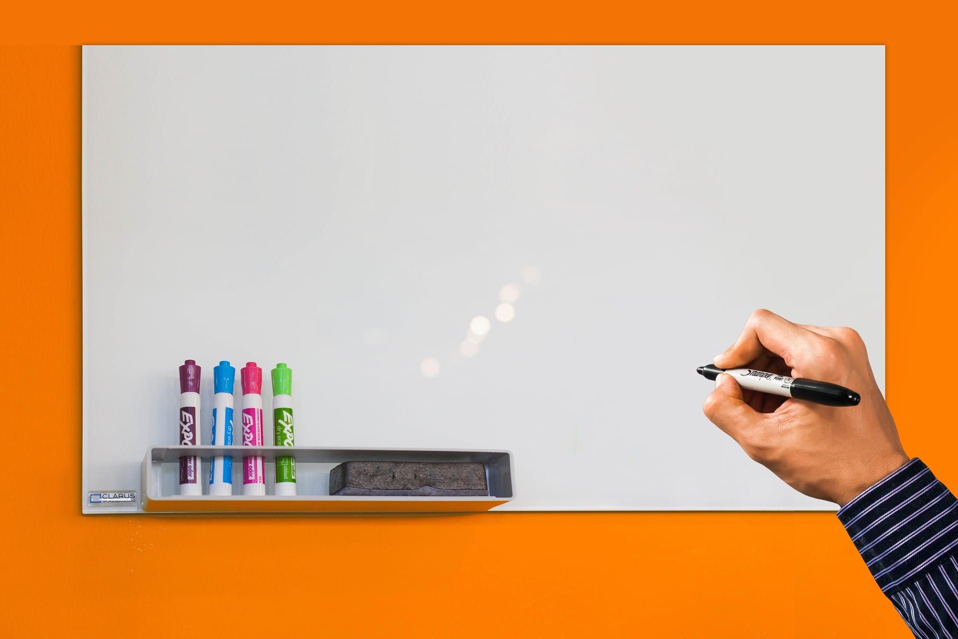 a blank whiteboard against an orange wall with a hand prepared to write on it