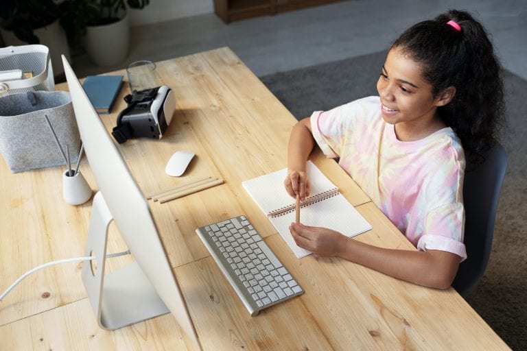 smiling girl sitting at desk looking at computer and taking notes