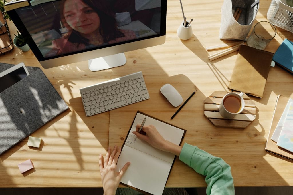 person taking notes in a notebook while watching a computer