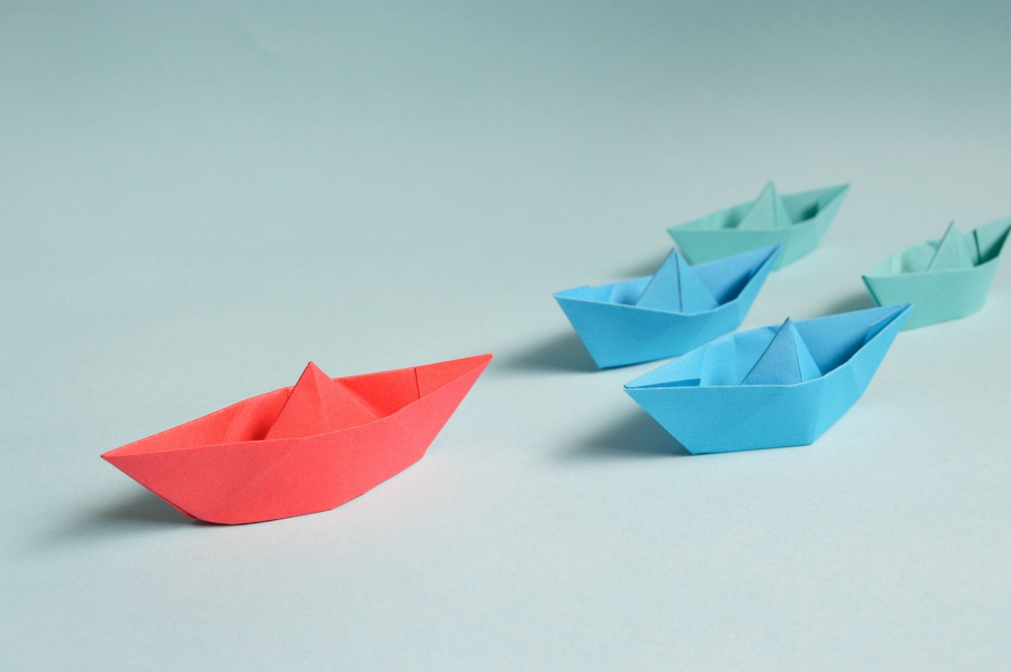 red paper boat leading blue and green paper boats